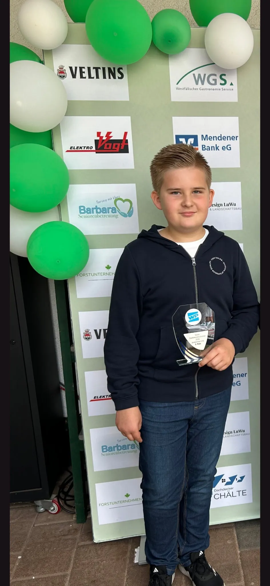 Maximilian Merse mit Pokal vor der Sponsorenwand